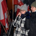Dwie dziewczynki podczas wykonywania utworu na tle biało-czerwonych i powstańczych flag