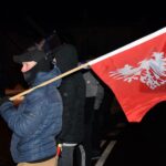 Młody mężczyzna trzymający na ramieniu flagę Powstania Wielkopolskiego