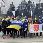 Grupa osób z flagami Ukrainy i Gminy Strzałkowo, w tle mural upamiętniający Powstanie Wielkopolskie