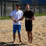 Dwóch młodych chłopaków w sportowych strojach podaje sobie ręce na boisku do siatkówki plażowej