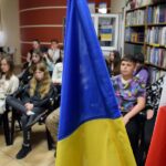 Czytelnia biblioteki. Na pierwszym planie flagi Polski i Ukrainy, w tle młodzież biorąca udział w spotkaniu