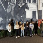Grupa młodzieży po zmroku stoi przy muralu upamiętniającym Powstanie Wielkopolskie
