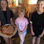 Dwie dziewczynki i chłopiec w pizzeri. Jedna z dziewczynek prezentuje pizzę w kształcie serca