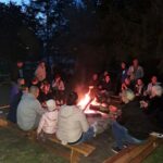 Grupa osób po zmroku siedzi przy rozpalonym ognisku