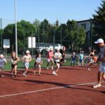 Dzieci z trenerem na korcie podczas tenisowej zabawy