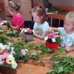 Trzy dziewczynki podczas warsztatów florystycznych układają kwiaty w ozdobnych pudełkach