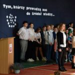 Zastępca wójta przemawia podczas Dnia Nauczyciela w Zespole Szkolno-Przedszkolnym w Wólce. Obok stoją uczniowie biorący udział w części artystycznej