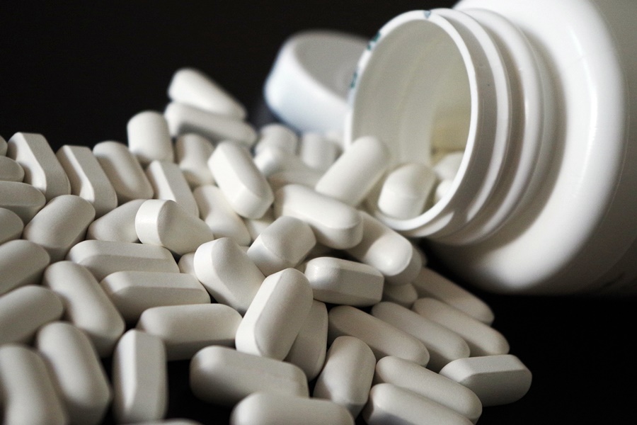 Białe tabletki wysypujące się z plastikowego opakowania