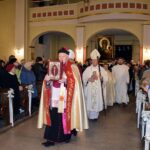 Dziekan strzałkowski trzymając lekcjonarz wchodzi do kościoła, za nim księża i służba liturgiczna oraz strażacy niosący obraz Matki Bożej