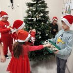 Kilkoro dzieci w czapkach Mikołajów ubiera choinkę