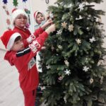 Trzech chłopców w czapkach Mikołajów przystraja choinkę