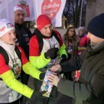 Zastępca wójta gminy wrzuca pieniądze do puszki WOŚP biegaczom Biegu z Pierwszej Stolicy do Stolicy
