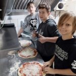 Trzech chłopców podczas przygotowania pizzy na warsztatach w pizzerii