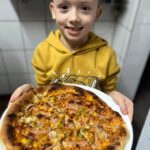 Uśmiechnięty chłopiec trzyma w rękach pizzę