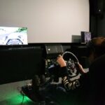 Chłopiec w goglach VR siedzi w rajdowym fotelu i gra w wyścigi samochodowe