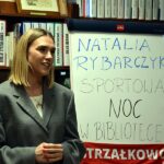 Bohaterka nocy w bibliotece - Natalia Rybarczyk na tle regału z książkami i tablicy z hasłem tegorocznej nocy w bibliotece