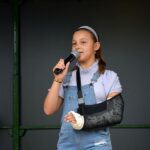 Dziewczyna z ręką w gipsie śpiewa do mikrofonu na scenie