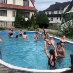 Kilkunastoosobowa grupa dzieci i młodzieży w strojach kąpielowych w odkrytym basenie