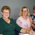 Trzy uśmiechnięte kobiety siedzą przy stole