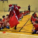 Św. Mikołaj z workiem prezentów przechodzi obok młodych piłkarzy przybijając z nimi piątkę