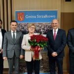 Teresa Jóźwiak z bukietem czerwonych róż pozuje do zdjęcia z wójtem, jego zastępcą, sekretarz Gminy i przewodniczącym Rady Gminy
