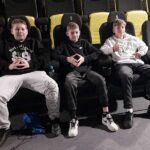 Trzech chłopaków siedzi na fotelach kinowych w pierwszym rzędzie