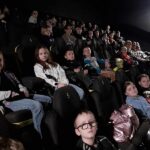 Uczestnicy wycieczki siedzą na fotelach w ciemnej sali kinowej