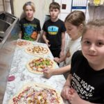 Dwóch chłopców i dwie dziewczynki przygotowują pizze w kuchni pizzerii podczas warsztatów