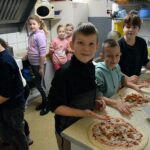 W kuchni pizzerii dzieci przygotowują pizze podczas warszatów