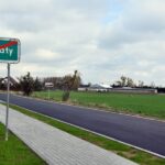 Fragment nowego chodnika i wymienionej nawierzchni drogi. Przy chodniku z lewej strony stoi znak z przekreśloną nazwą miejscowości Kornaty