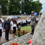 Delegacja szkoły - dyrektor i dwie uczennice, stoi przed pomnikiem z pochylonymi głowami