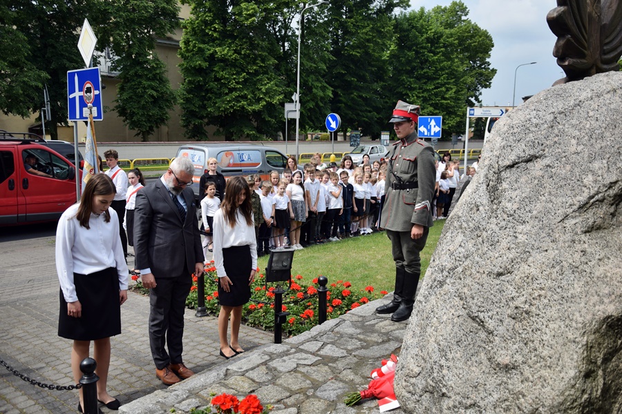 Delegacja szkoły - dyrektor i dwie uczennice, stoi przed pomnikiem z pochylonymi głowami