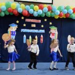 Grupa dzieci tańczy trzymając w rękach okrągłe, kolorowe lizaki