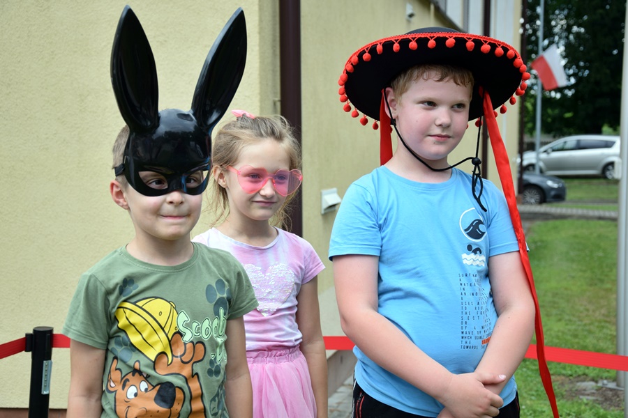 Trójka dzieci w przebraniach pozuje w fotobudce. Jeden z chłopców ma na głowie kapelusz, a drugi maskę królika