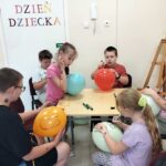 Kilkoro dzieci siedzi przy stole i maluje balony flamastrami