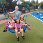 Cztery dziewczynki bujają się na huśtawce na placu zabaw