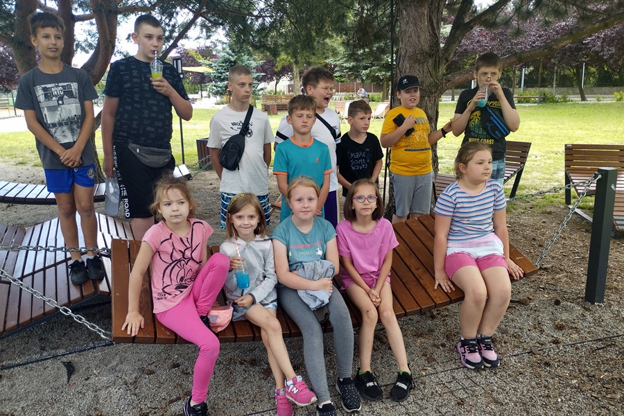 Grupa dzieci pozuje do zdjęcia w Strzałkowskiej Strefie Relaksu. Dziewczynki w pierwszym rzędzie siedzą na drewnianym hamaku
