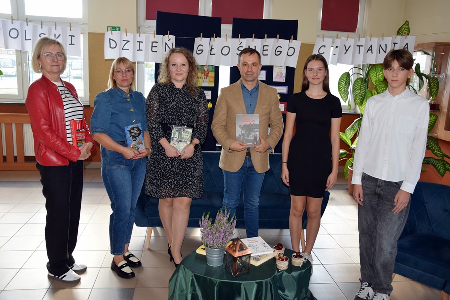 Zaproszeni goście oraz dwoje uczniów pozują do wspólnego zdjęcia na tle napisu Ogólnopolski dzień głośnego czytania