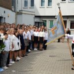 Na dziedzińcu ZSP Strzałkowo poczet sztandarowy stoi na przeciwko stojących uczniów