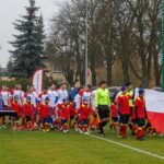 Zawodnicy obu drużyn wchodzą na boisku. Na przodzie zawodnicy młodzieżowi niosą biało-czerwoną flagę
