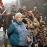 Dwoje dorosłych i dwoje dzieci - uczestnicy uroczystości. Za nimi na koniach mężczyźni w powstańczych mundurach